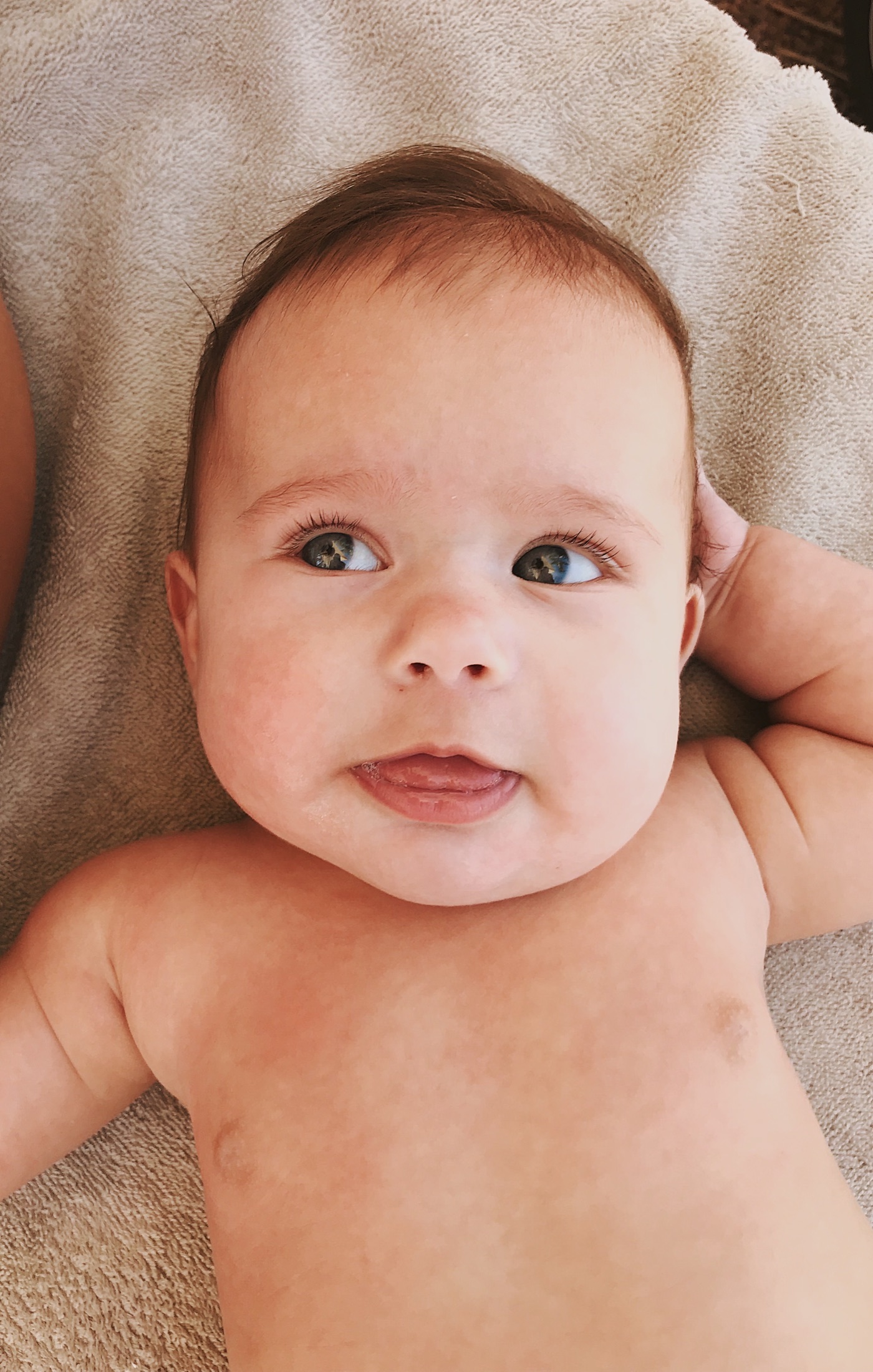 A baby rests on a soft blanket, looking towards the light.